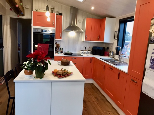 Vibrant orange kitchen complemented by the beautiful rustic wooden floor 